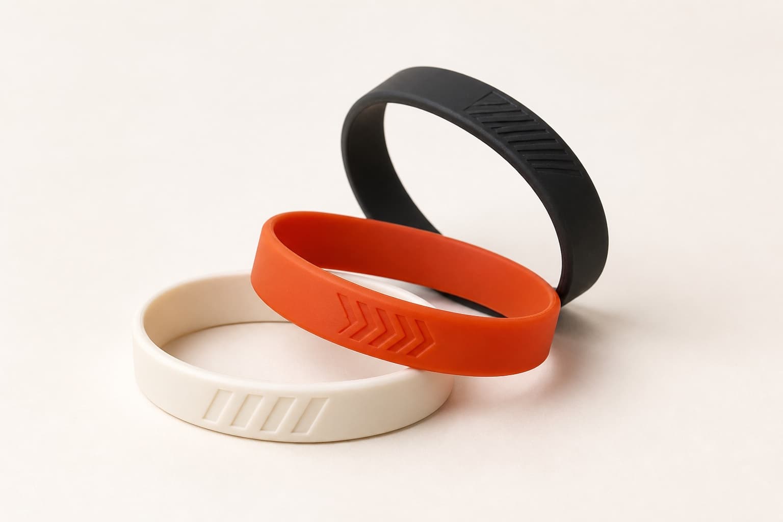 Trois bracelets en silicone, noir, orange et crème, avec un motif gravé en creux