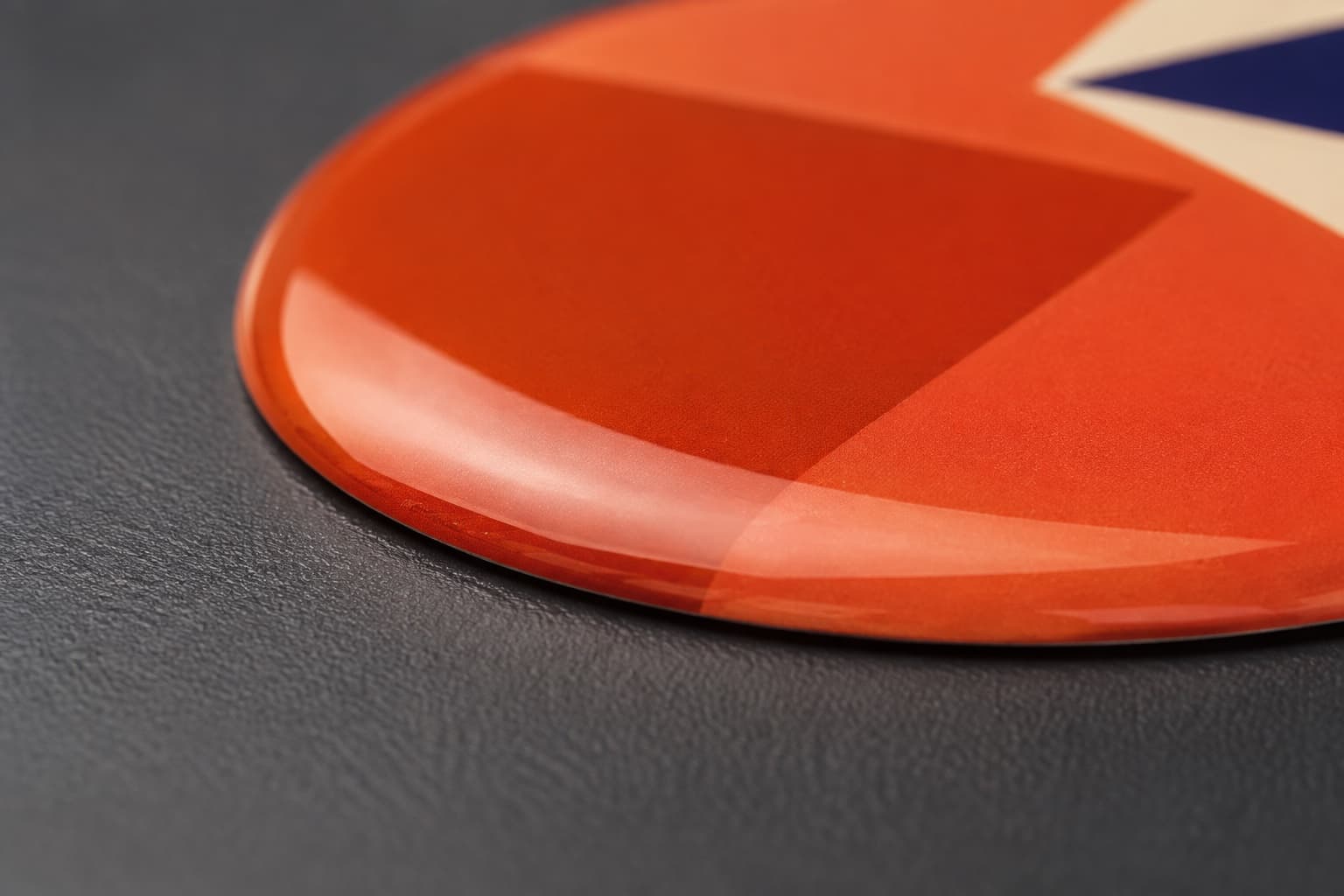 Extreme macro of the edge of a resin domed sticker showing the thick clear epoxy dome over an orange printed base